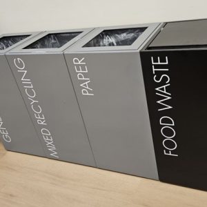 Recycling bin for offices in a row black and grey with white lettering. Office recycling bins
