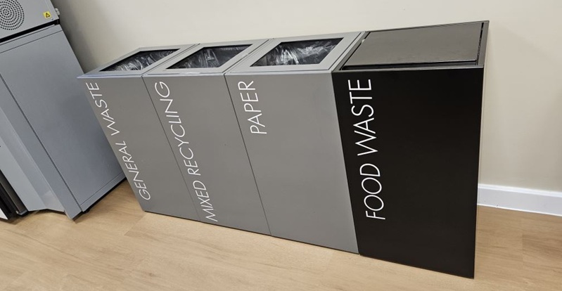 Recycling bin for offices in a row black and grey with white lettering. Office recycling bins