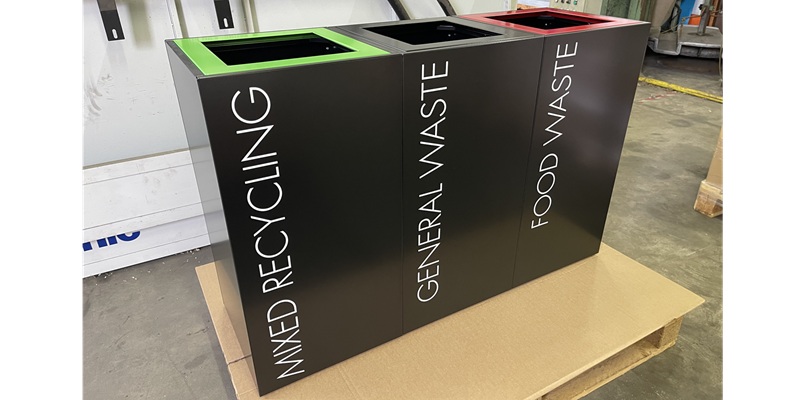 office recycling bins in a row with coloured tops and lettering to indicate waste stream
