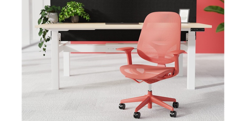 mesh office chair in coral with matching base in office in front of office desk