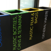 row of black office recycling bins with coloured tops and stickers