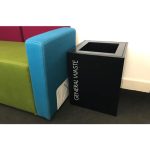 short black office recycling bin by side of sofa.