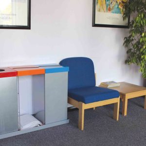 3 office recycling bins with coloured tops for different waste. In reception area with blue fabric reception chair and coffee table