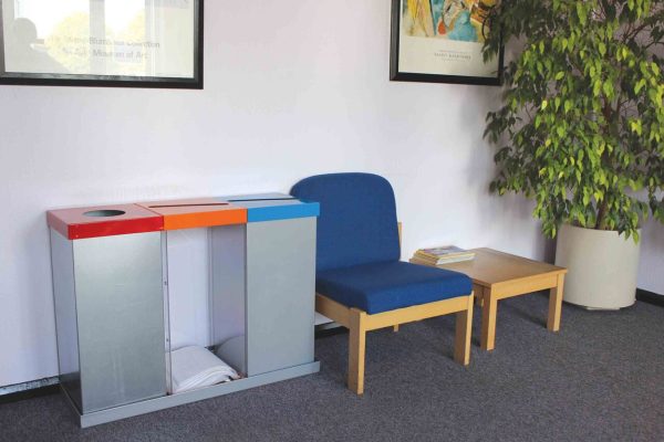 3 office recycling bins with coloured tops for different waste. In reception area with blue fabric reception chair and coffee table