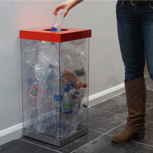 transparent office recycling bin full with plastic bottles with red top and someone placing a bin in the top.