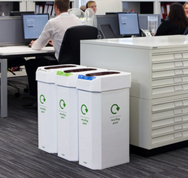 office scene with 3 cardboard office recycling bins at end of office storage with people in background